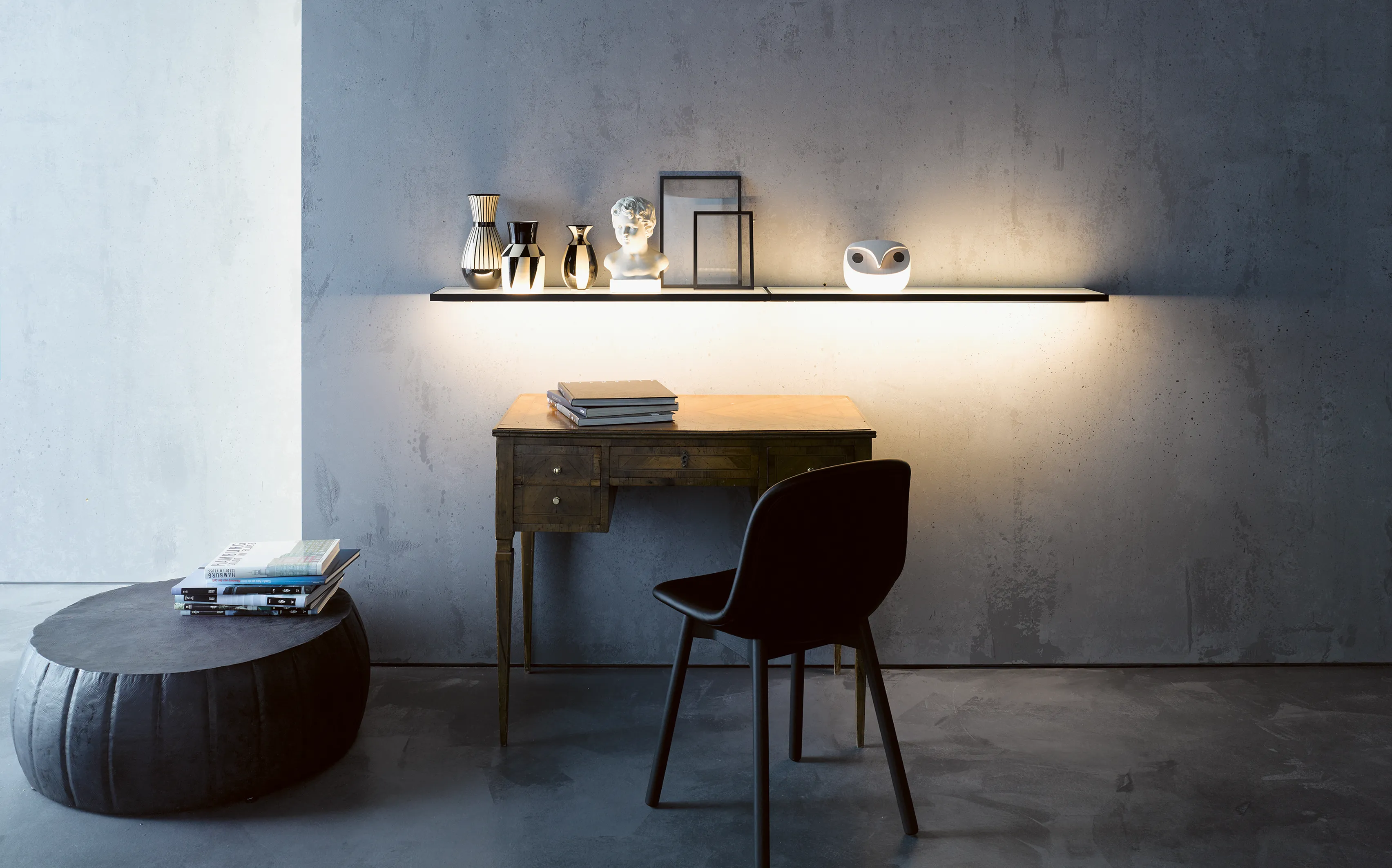 Schreibtisch mit beleuchteter Glasablage GERA Sunrise vor einer grauen Betonwand.