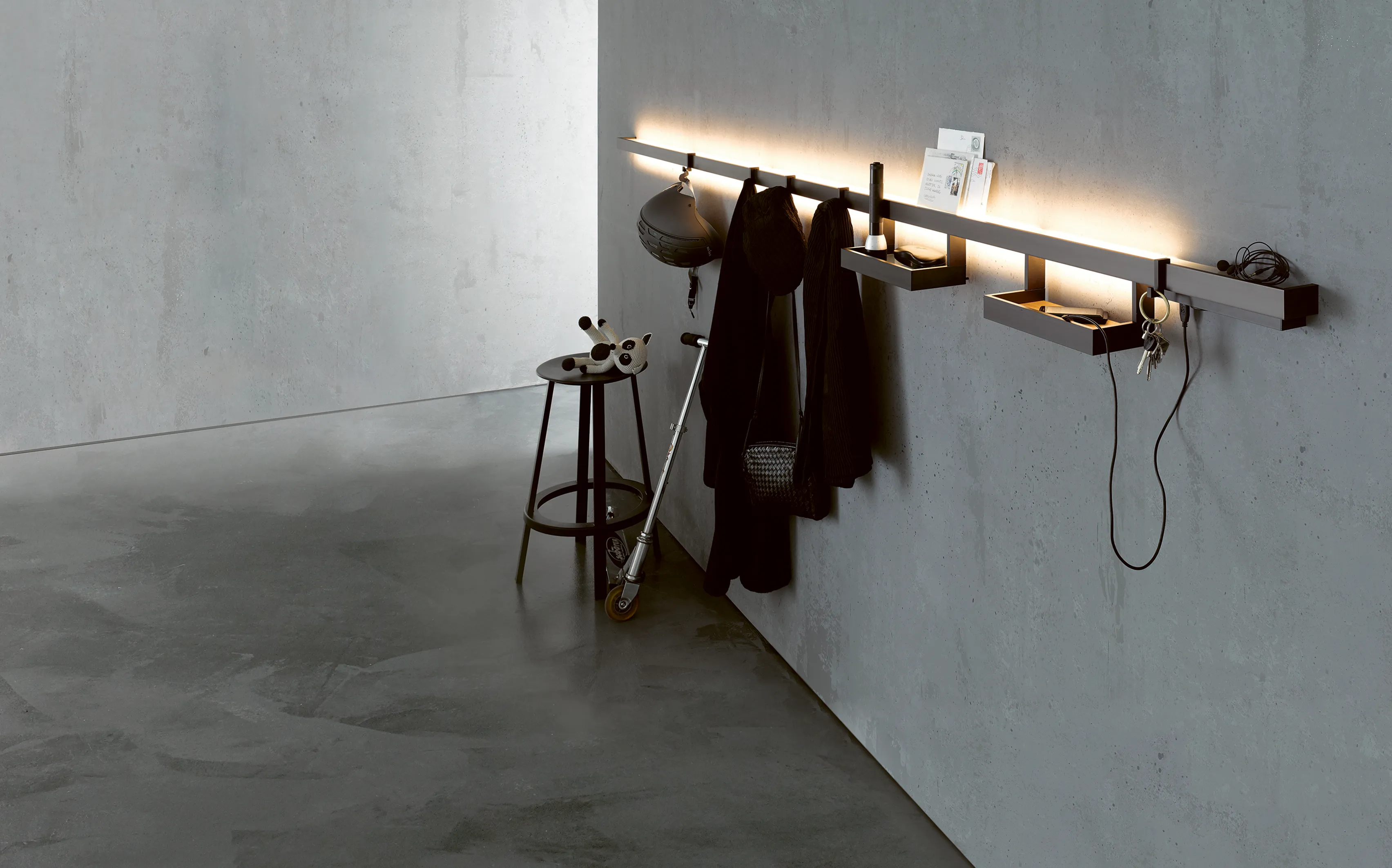 Beleuchtete Lichtreling GERA Line Up mit Ablagefächern und Haken an einer grauen Betonwand.