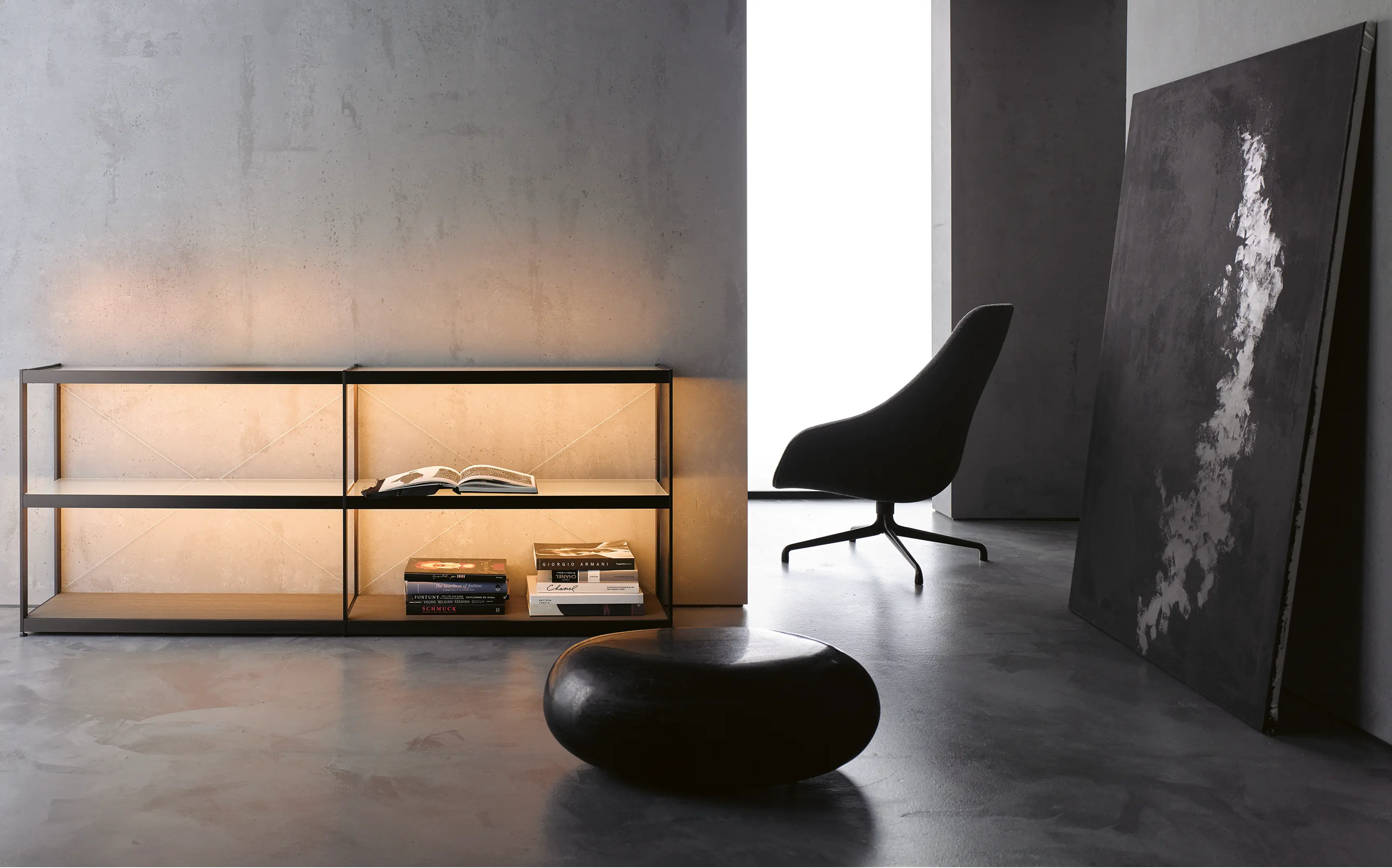 Minimalistisches Wohnzimmer mit beleuchtetem Sideboard GERA Item Twin, schwarzem Sessel und abstraktem Gemälde, an der Wand lehnend.