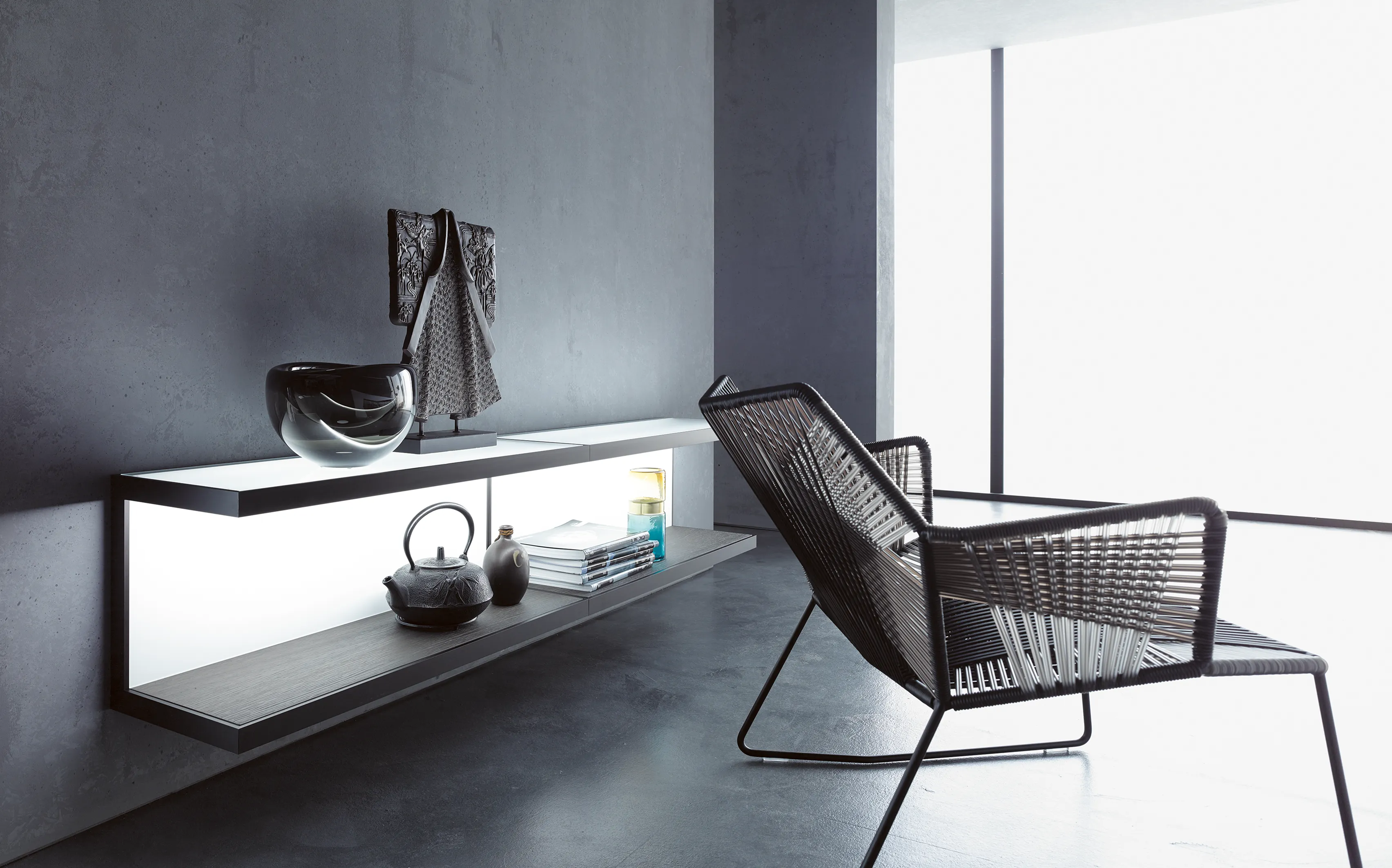 Modernes Wohnzimmer mit beleuchteten GERA Scoop Wandregalen, Design-Sessel aus Geflecht und asiatischen Dekorationsobjekten.