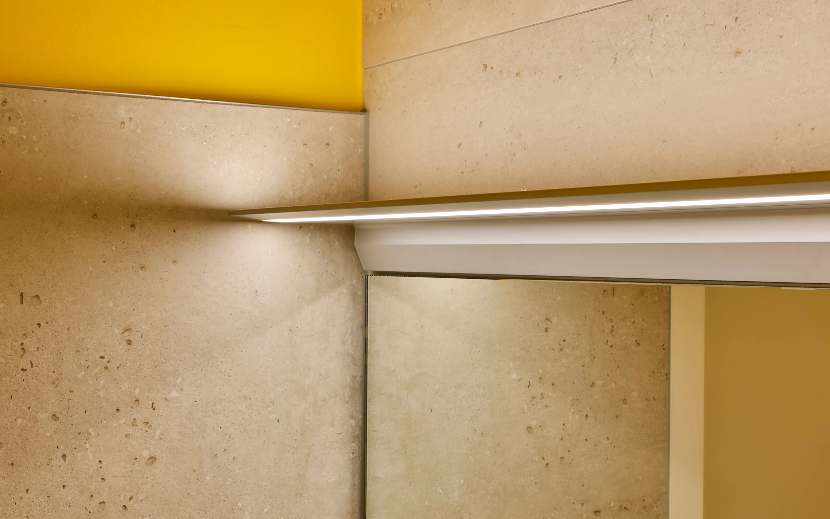 Indirekt beleuchtetes Lichtbord GERA Feature vor einer Wand aus Naturstein mit gelbem Akzent.