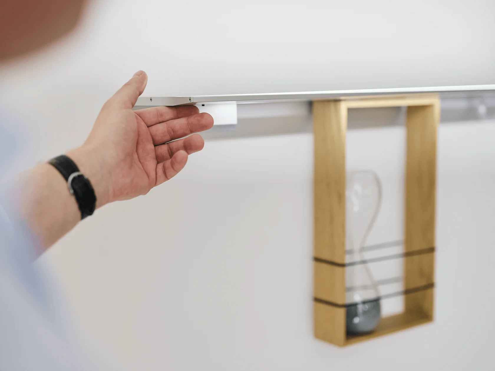 Hand greift unter die Möbelleuchte GERA Feature um den Sensorschalter zu bedienen.