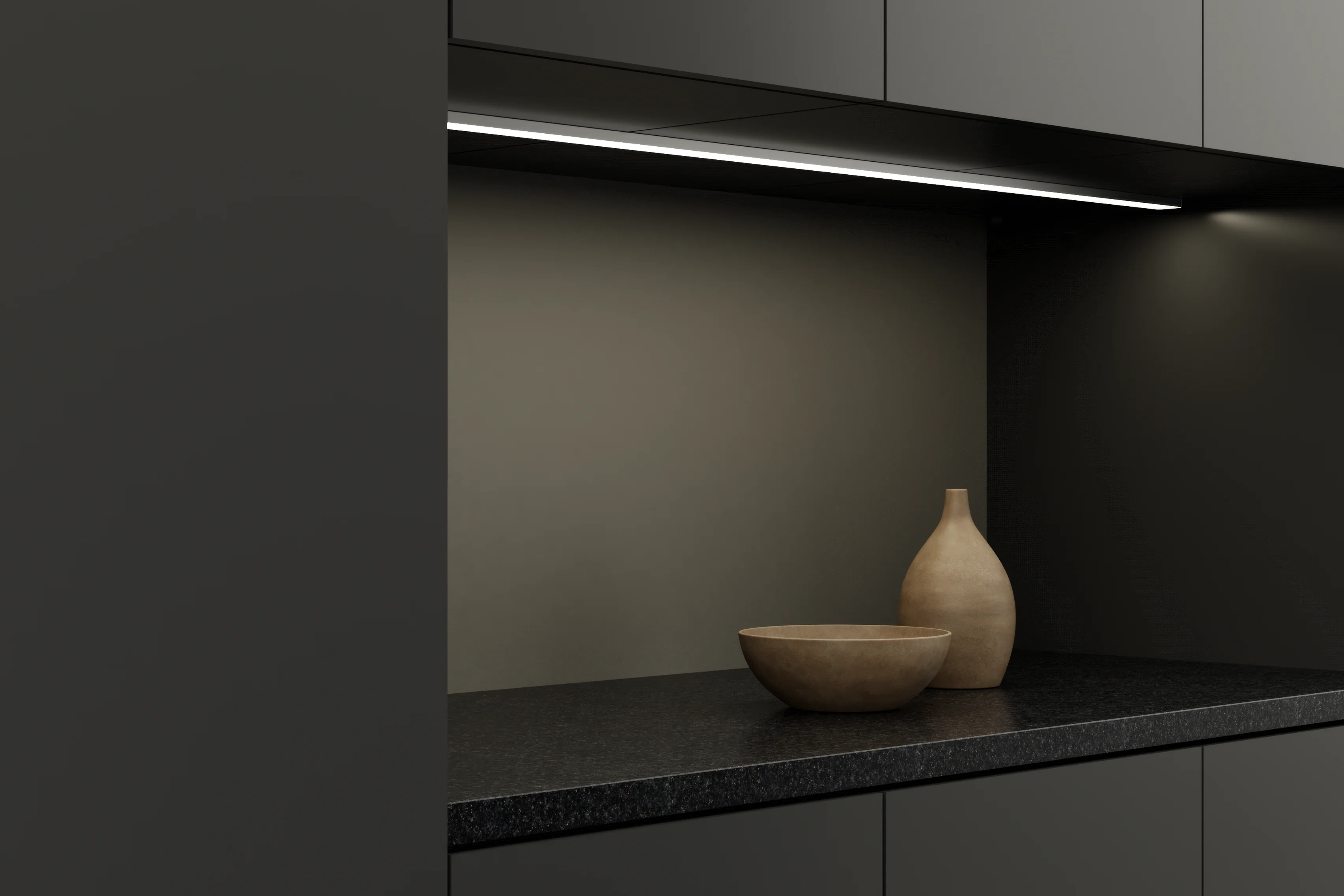 Gera Unterbauleuchte 32×10 montiert unter einem Küchenschrank, eine dunkle Granitarbeitsfläche mit Schale und Vase beleuchtend.