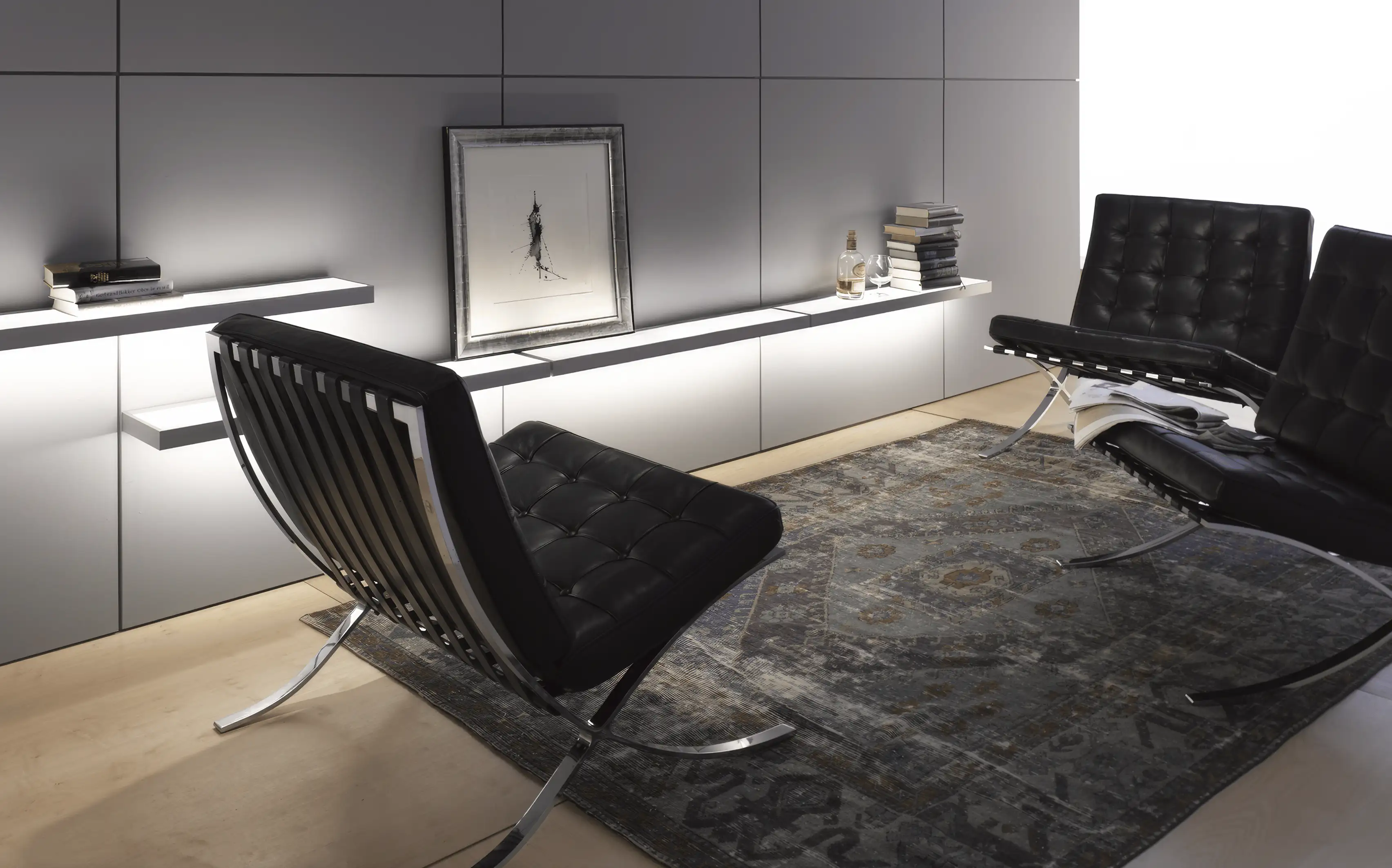 Modernes minimalistisches Wohnzimmer mit zwei schwarzen Barcelona-Sesseln auf einem orientalischen Teppich vor beleuchteten GERA Add Lichtbords.