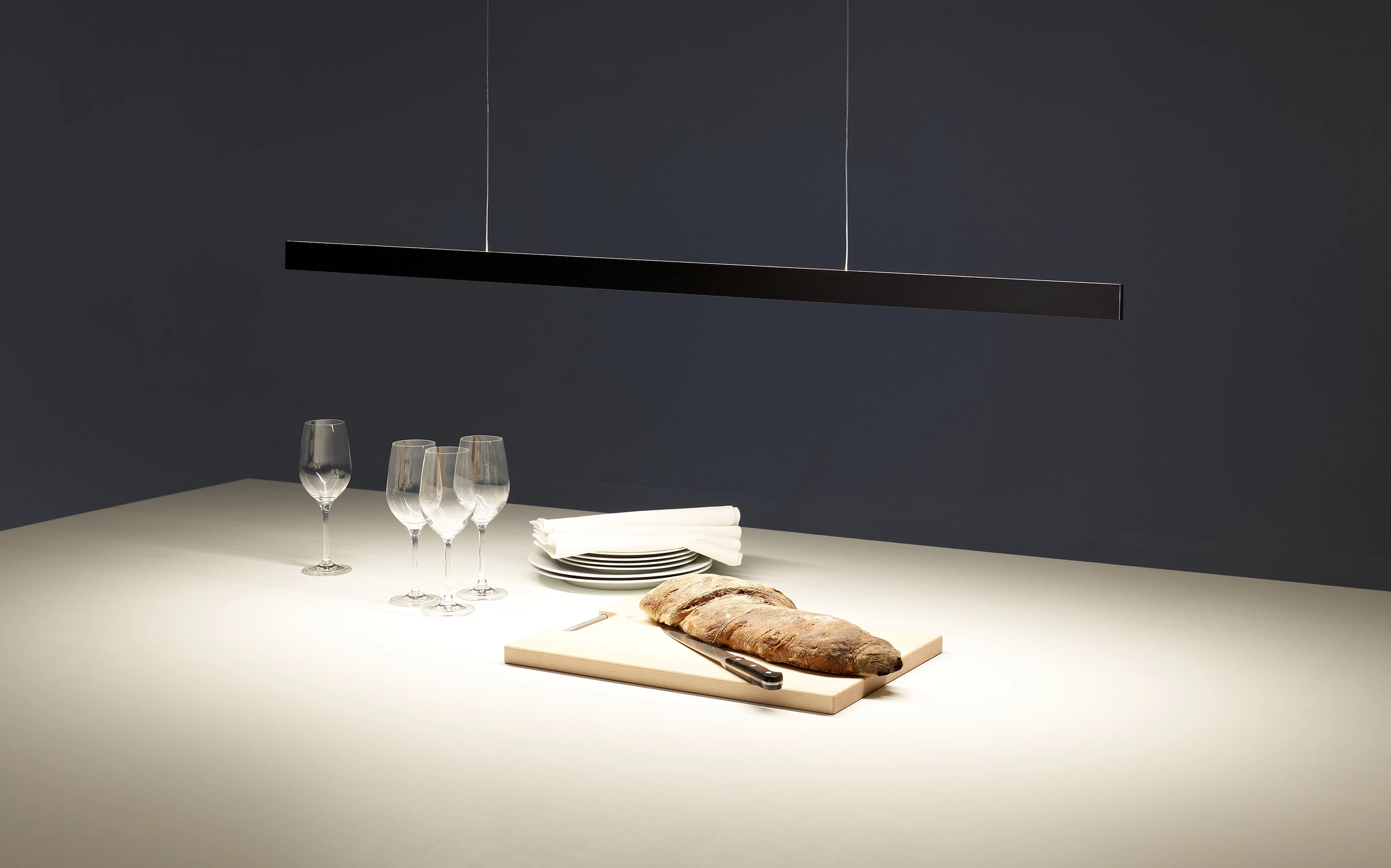 Minimalistische schwarze Pendelleuchte GERA Solid über einem gedeckten Esstisch mit Brotleib und Weingläsern.