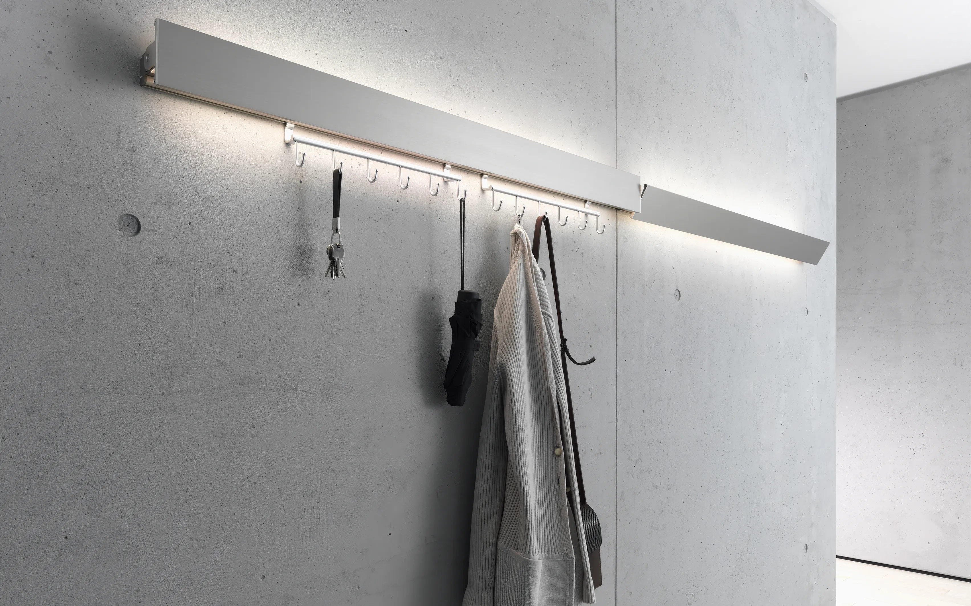 Garderobenleuchte GERA Hook aluminium mit Hakenleiste an einer Sichtbetonwand.
