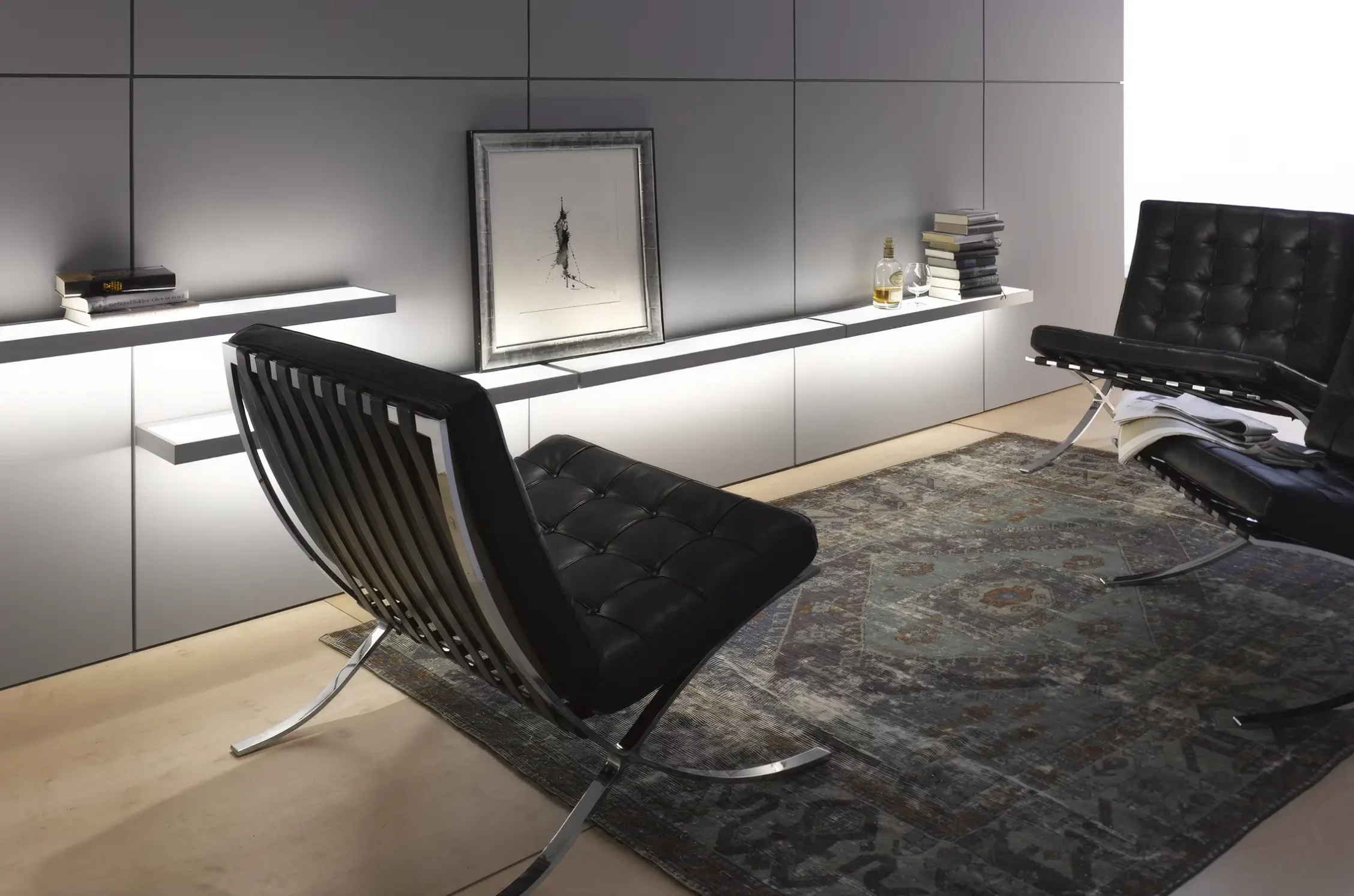 Modernes minimalistisches Wohnzimmer mit zwei schwarzen Barcelona-Sesseln auf einem orientalischen Teppich vor beleuchteten GERA Add Lichtbords.