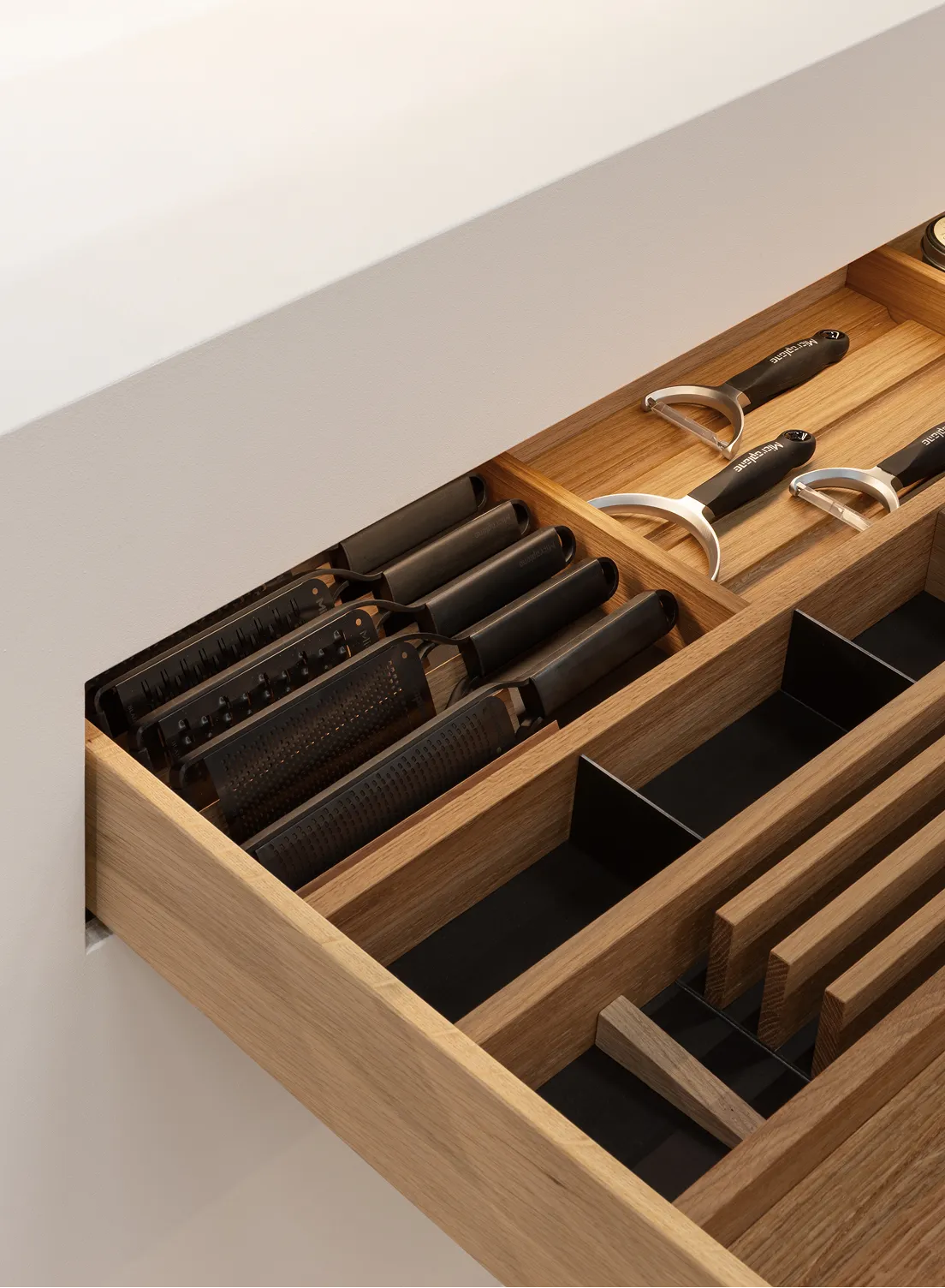 Sortierte Küchenreiben und Sparschäler in einem hölzernen Schubladen-Inlay beleuchtet von einer GERA Auszugbeleuchtung.