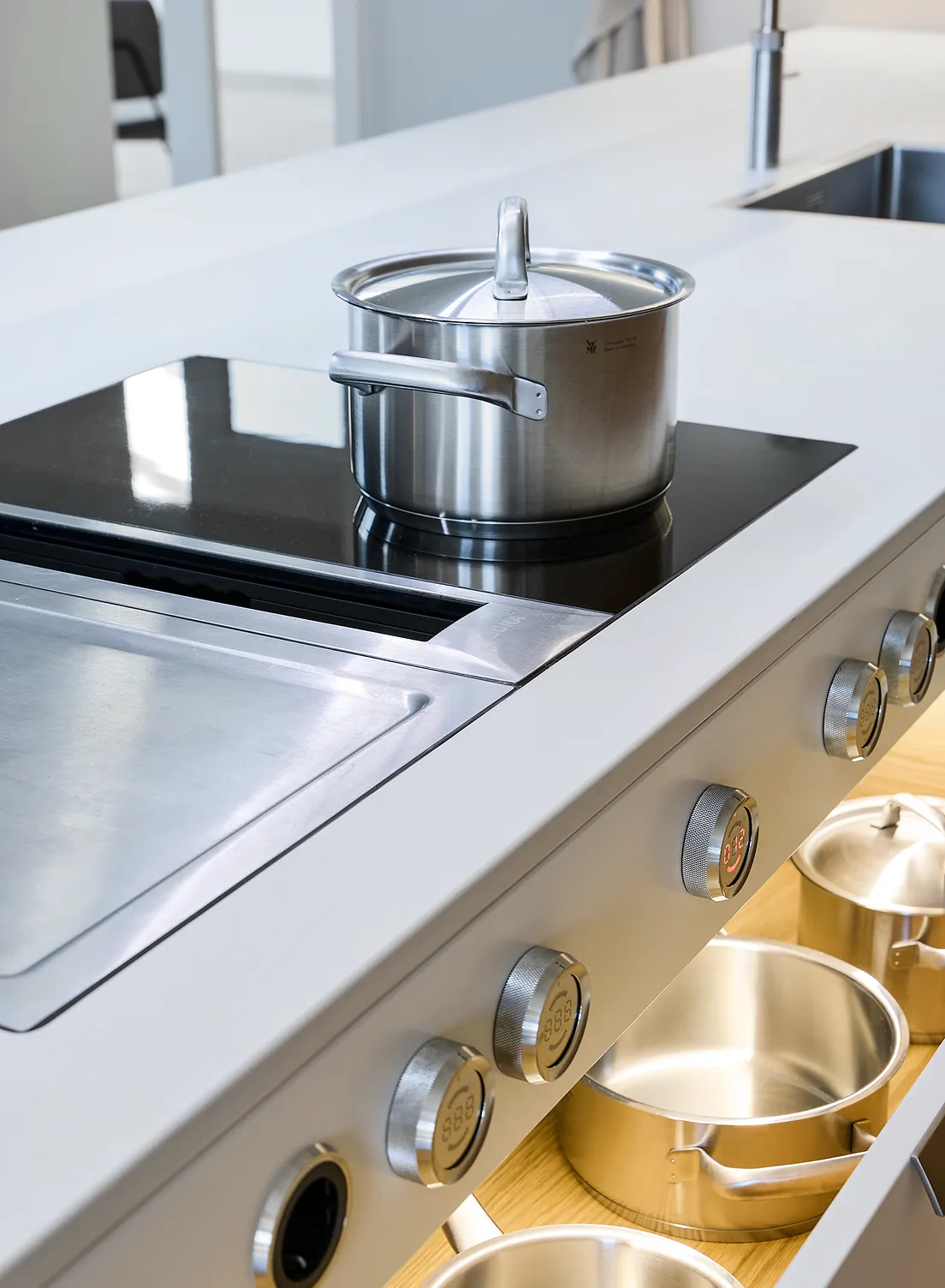 Moderner Induktionsherd mit Edelstahltopf und integriertem Dunstabzug sowie mit der GERA Auszugbeleuchtung beleuchteten Schubladen mit Kochgeschirr.