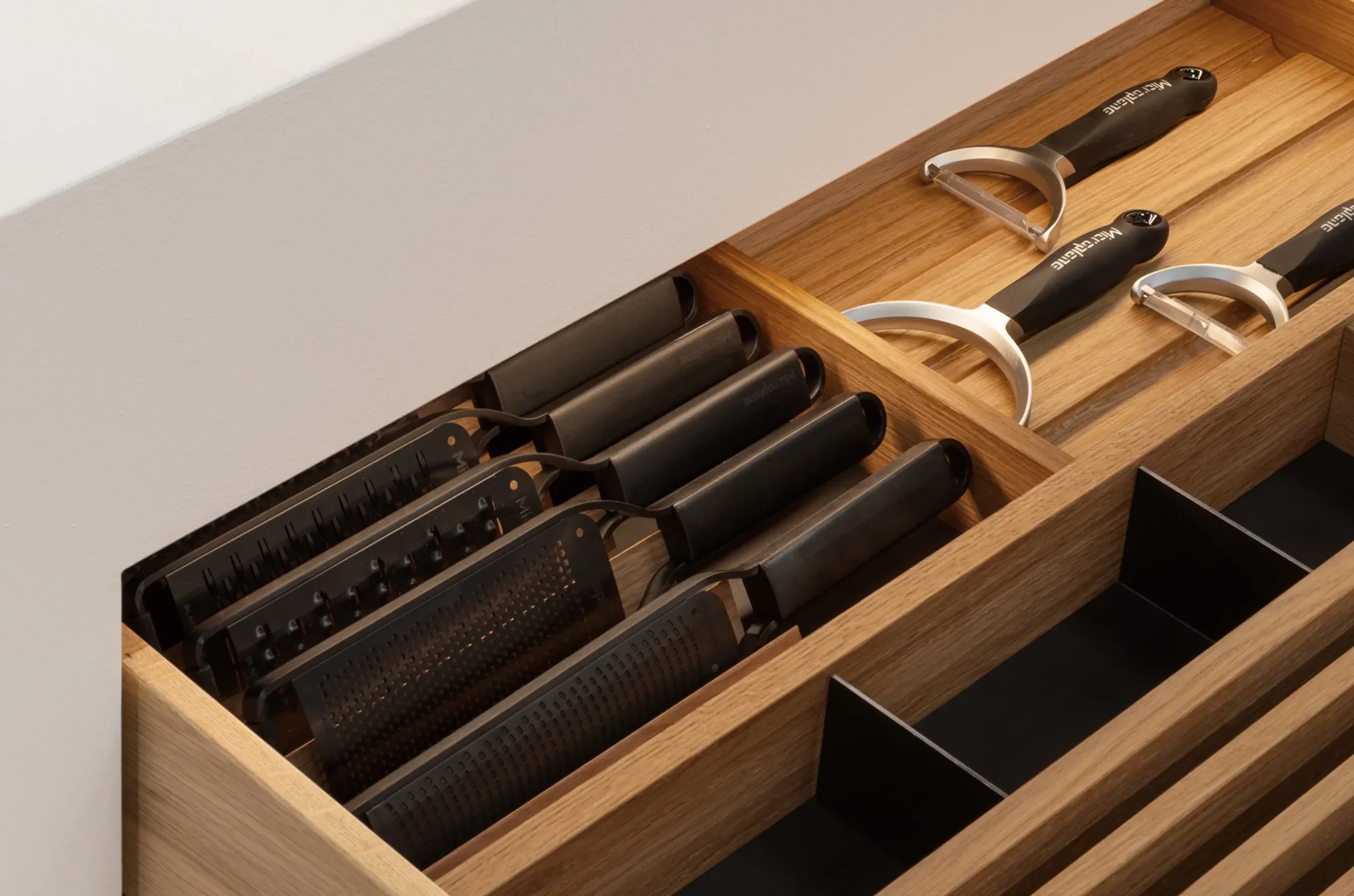 Sortierte Küchenreiben und Sparschäler in einem hölzernen Schubladen-Inlay beleuchtet von einer GERA Auszugbeleuchtung.