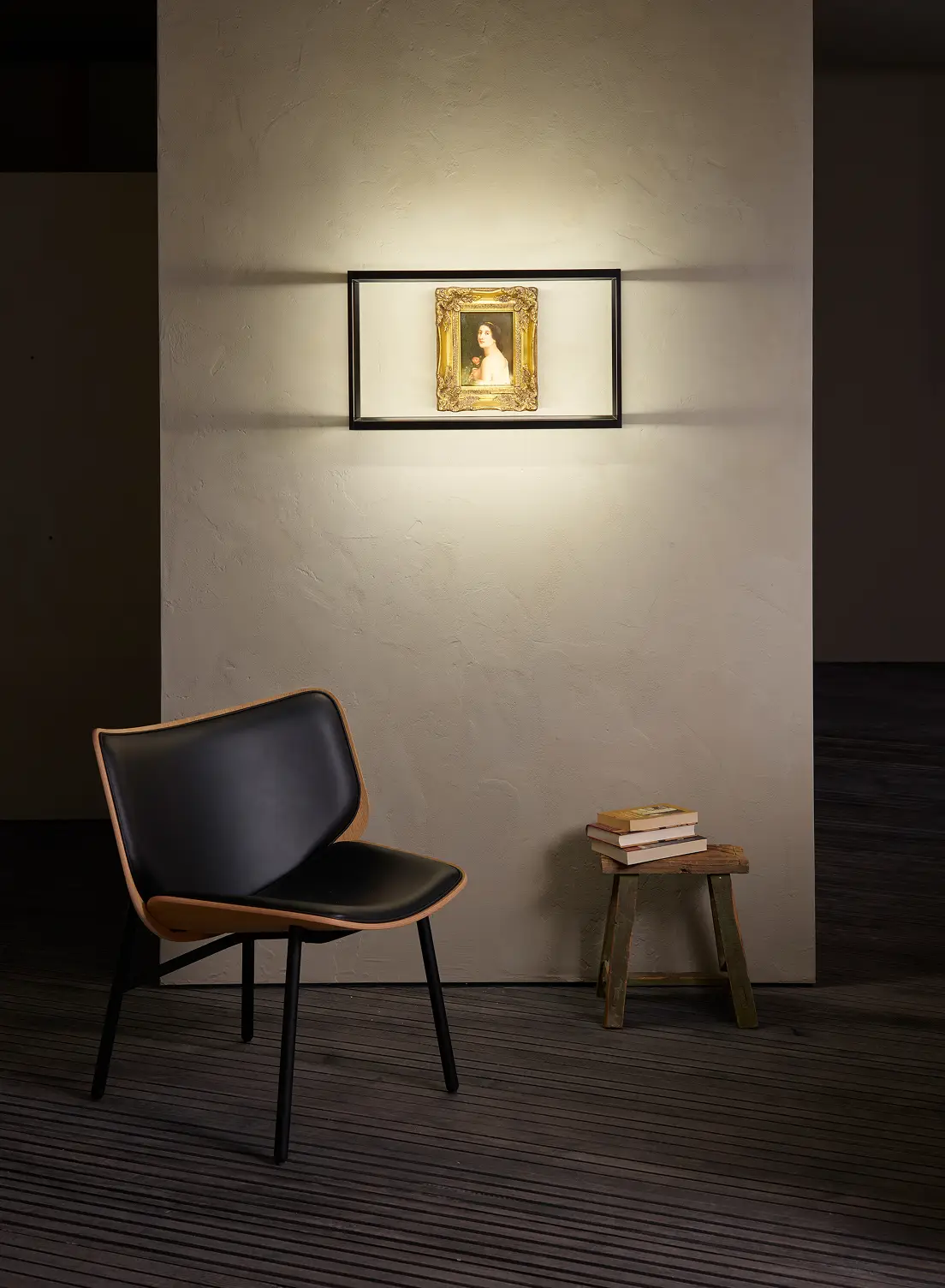 Moderner Sessel und ein kleiner Hocker mit Büchern unter einem beleuchteten Wandregal GERA Cube, das ein Gemälde umrahmt.