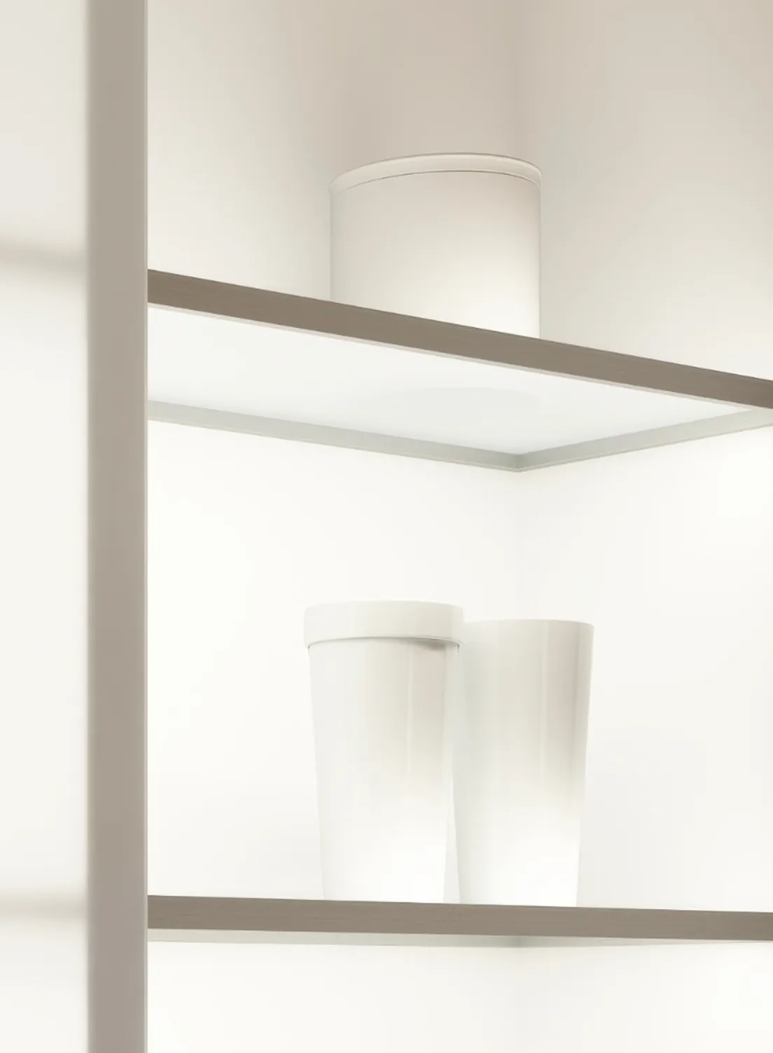 Beleuchtetes, minimalistischer Küchenschrank mit Glastüren. Gläser, Tassen und ein Glasbehälter gefüllt mit Kaffeebohnen stehen auf den GERA Einlegeböden.