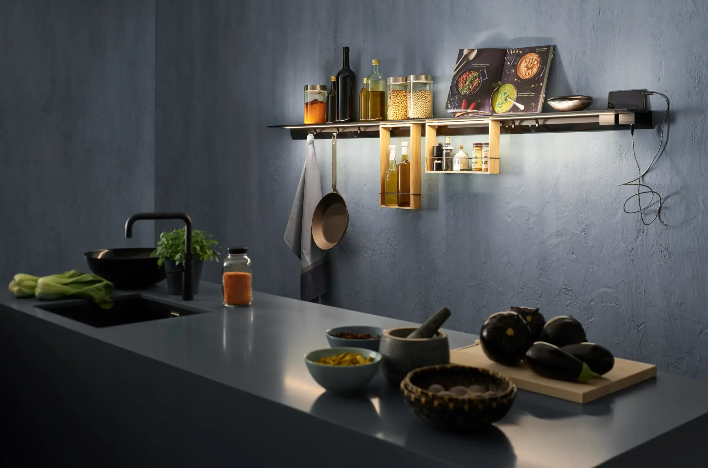 Moderne Küchenzeile mit beleuchtetem Lichtbord GERA Feature, Kochutensilien und Zutaten auf einer dunklen Arbeitsplatte.