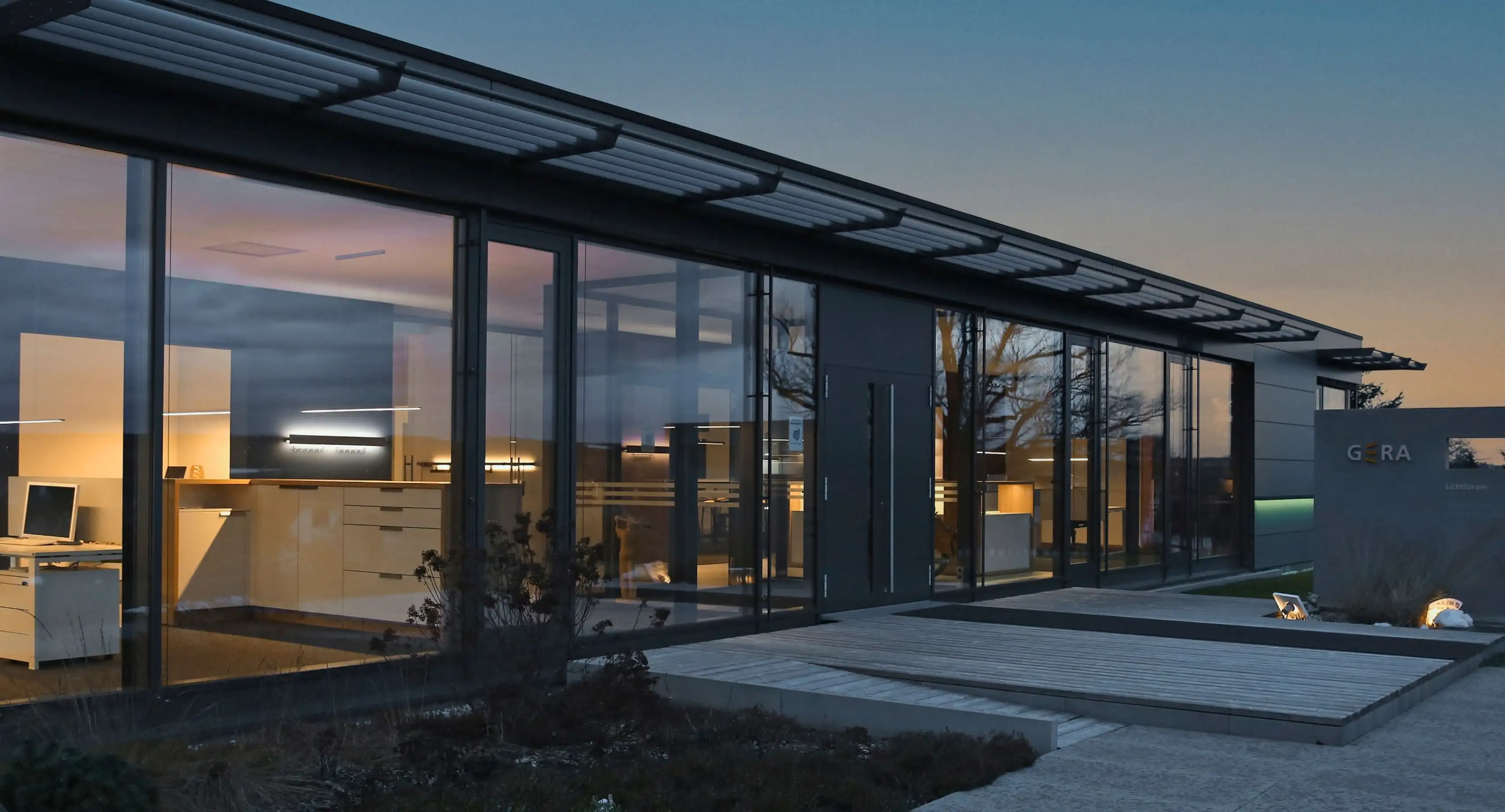 Moderne Glasarchitektur des GERA Lichtforums in St. Gangloff bei Dämmerung mit Blick auf beleuchtete Innenräume.