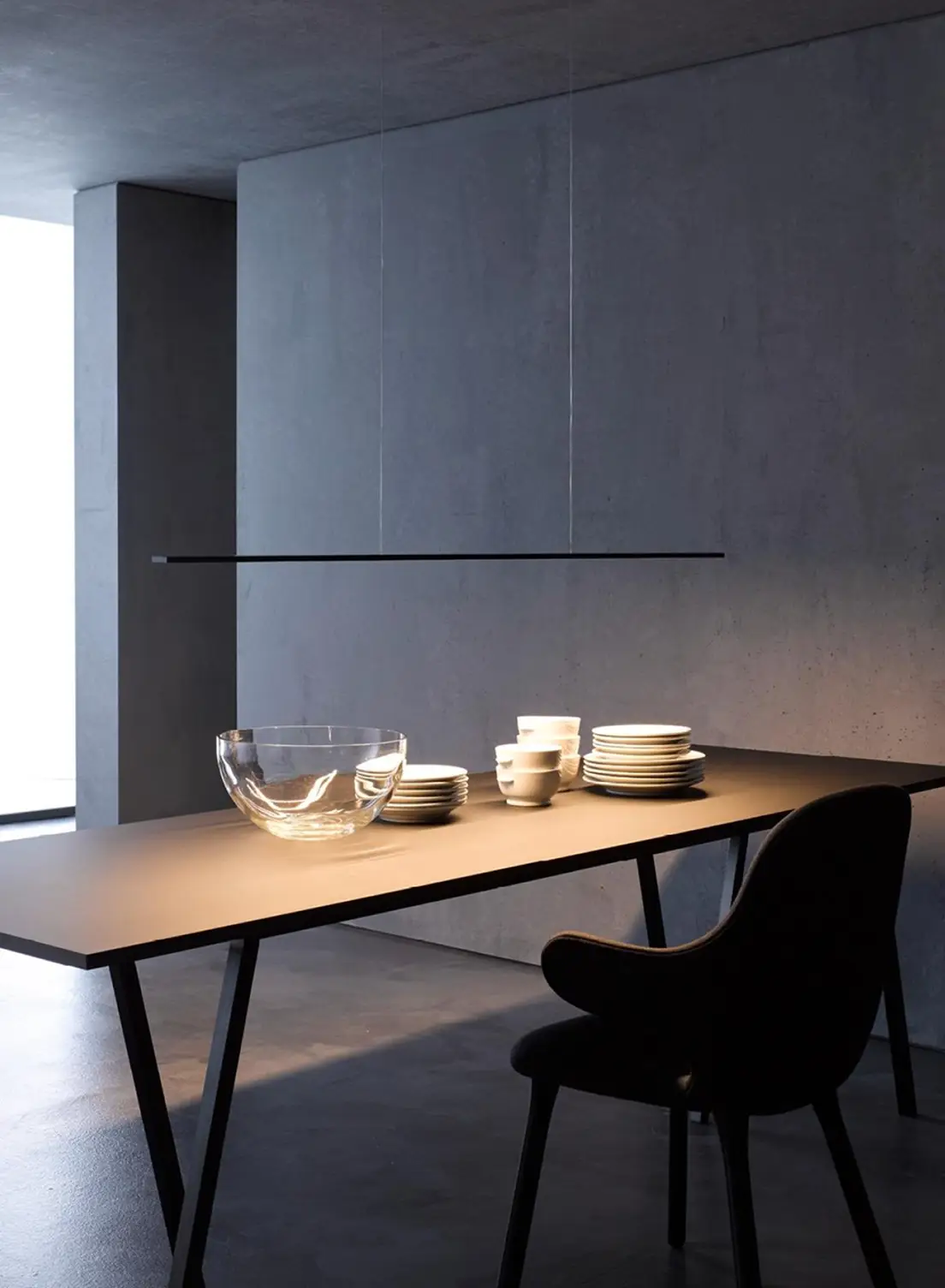 Minimalistischer Esstisch beleuchtet mit Pendelleuchte GERA Horizon in dunklem, betonfarbenem Raum.
