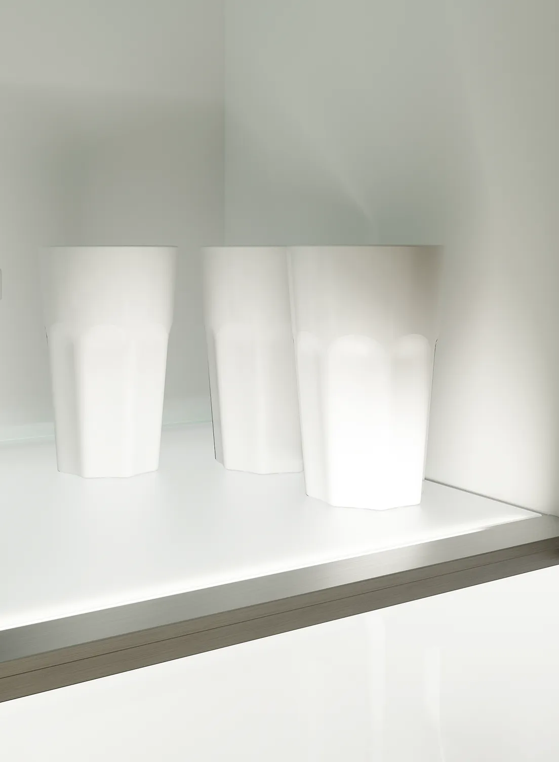 Beleuchtetes, minimalistischer Küchenschrank mit Glastüren. Gläser, Tassen und ein Glasbehälter gefüllt mit Kaffeebohnen stehen auf den GERA Einlegeböden.