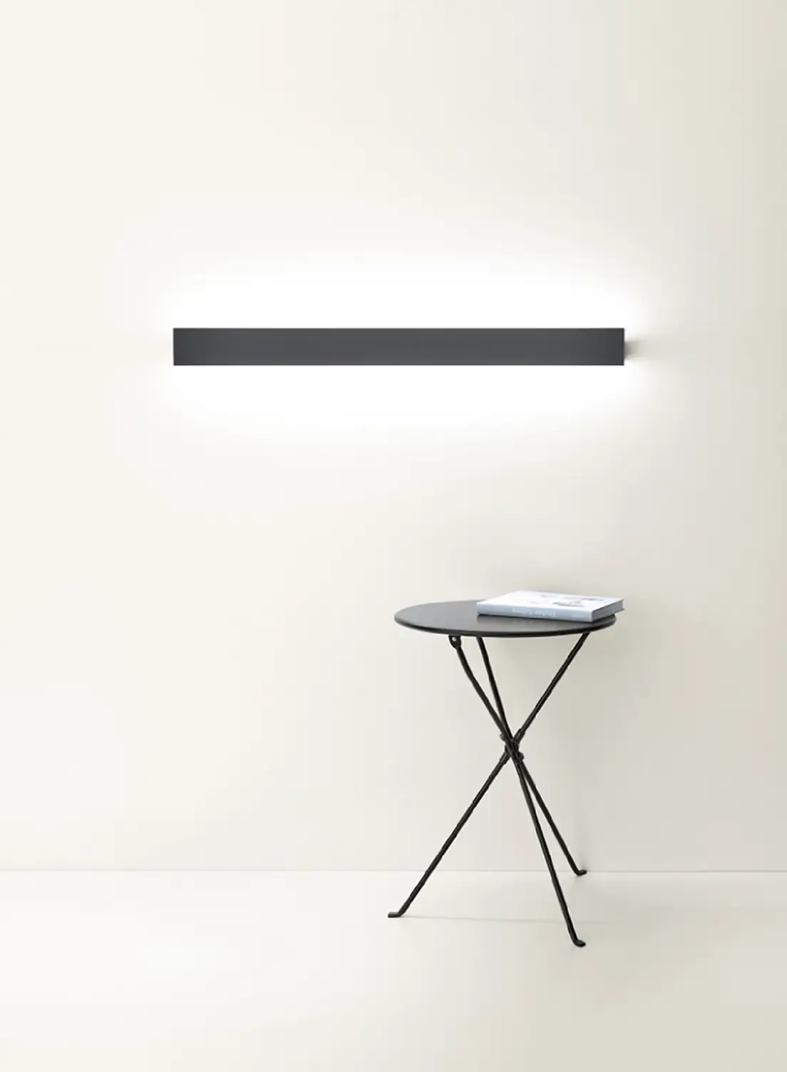 Schwarze Wandleuchte GERA Slant über einem kleinen runden Beistelltisch in hellem Raum.