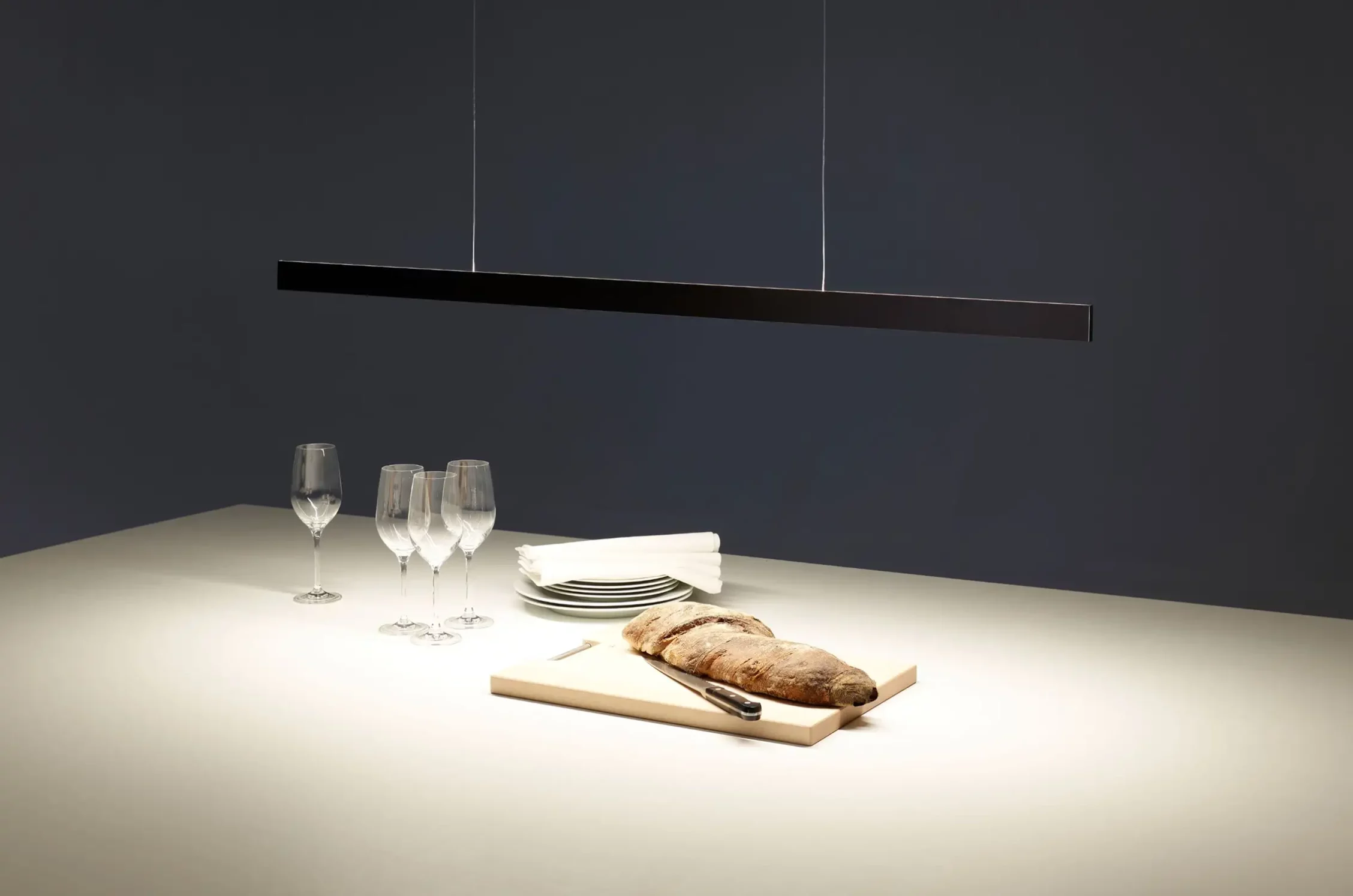 Pendelleuchte GERA Solid über einem gedeckten Tisch mit Weingläsern, Tellern und frischem Brot auf einem Schneidebrett.