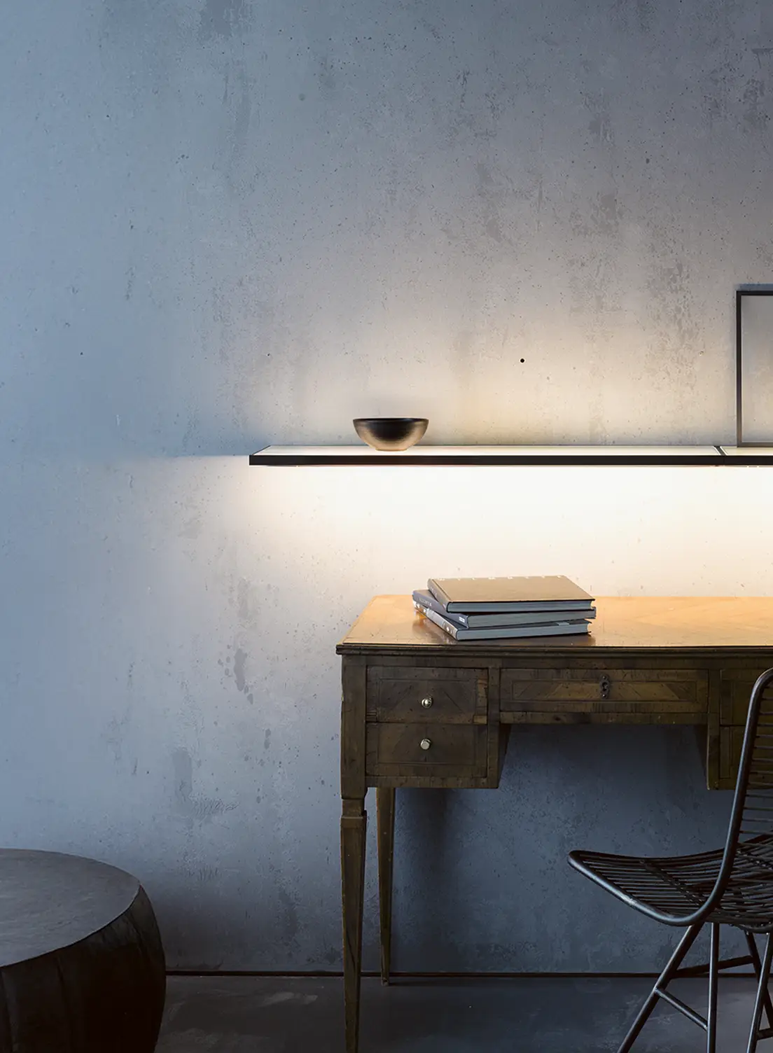 Schreibtisch mit beleuchteter Glasablage GERA Sunrise vor einer grauen Betonwand.