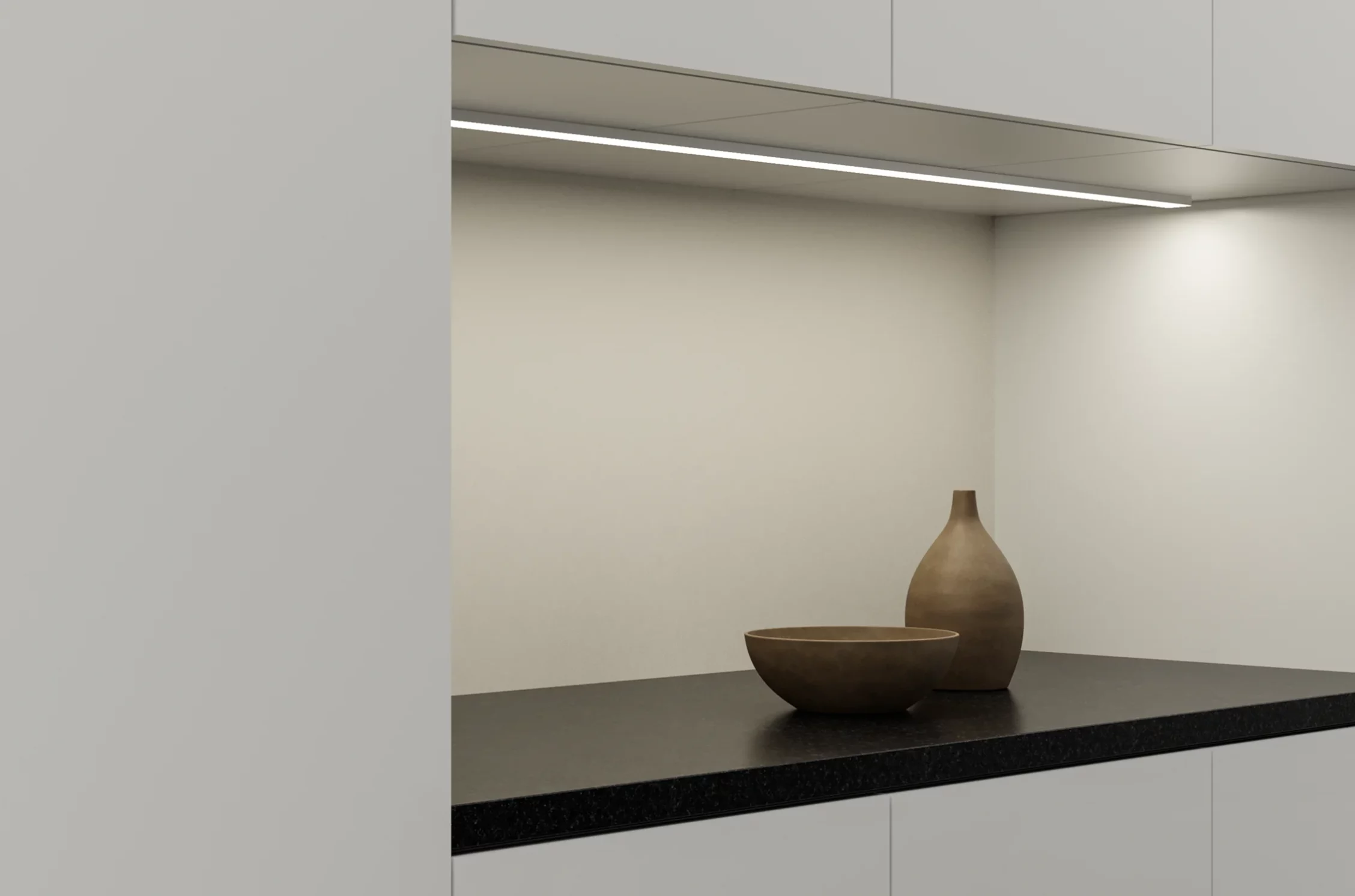 Gera Unterbauleuchte 32×10 montiert unter einem Küchenschrank, eine dunkle Granitarbeitsfläche mit Schale und Vase beleuchtend.