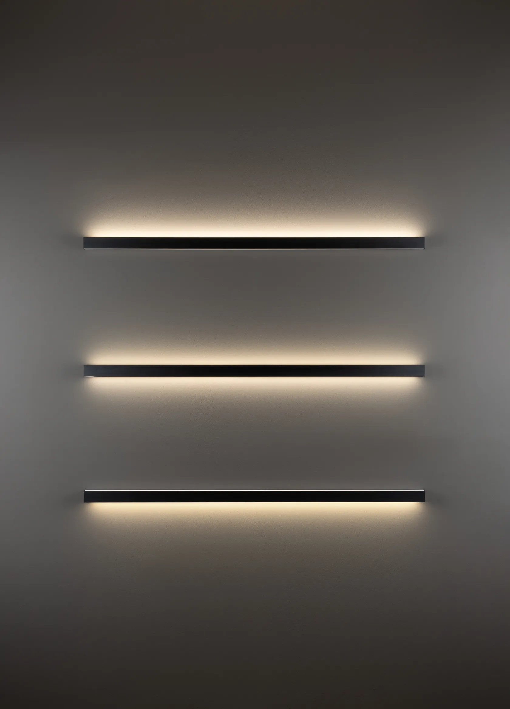 Drei horizontal übereinander installierte GERA Quadra Wall Wandleuchten werfen Licht nach oben und unten auf eine dunkle Wand.