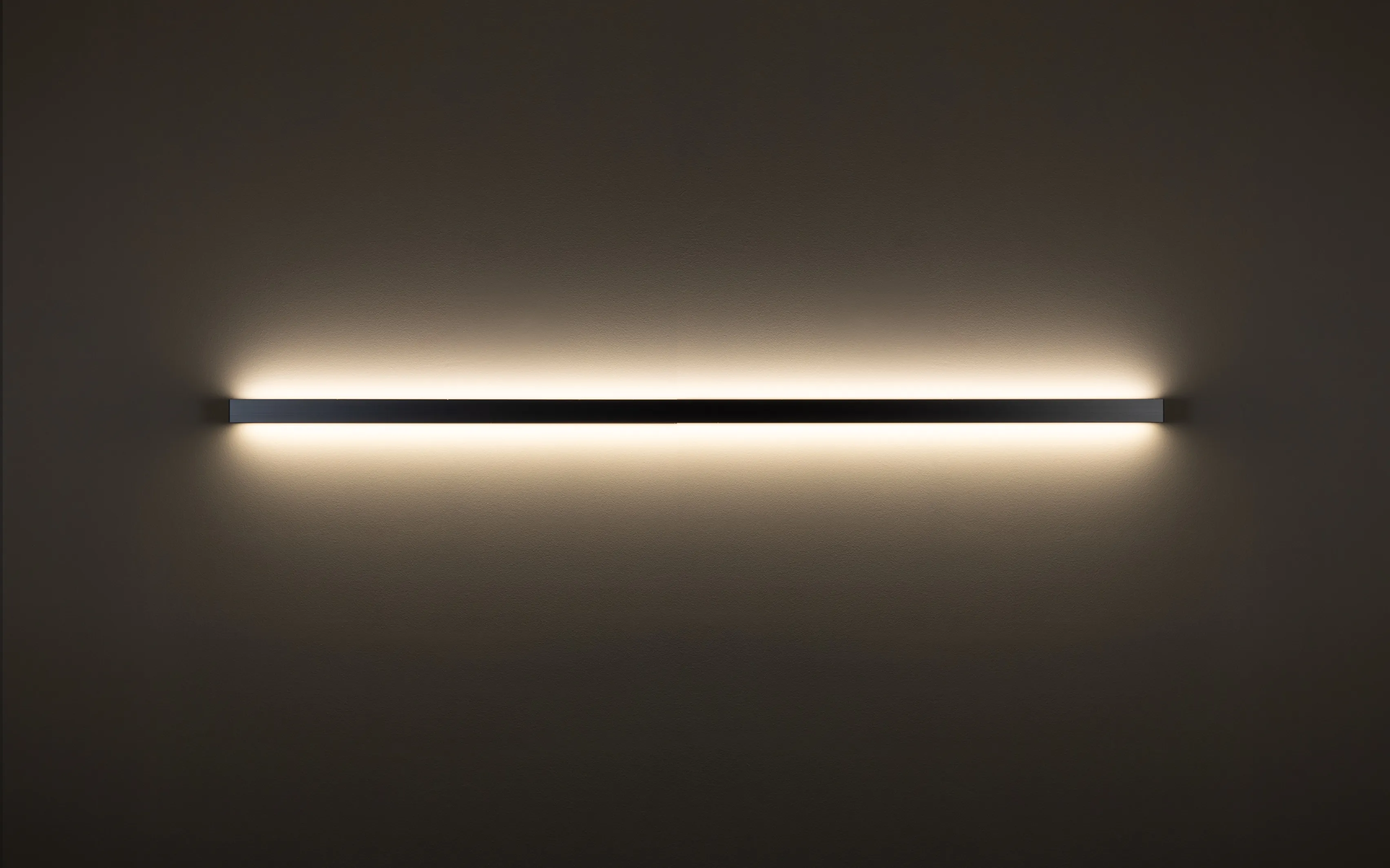 Horizontal installierte Wandleuchte GERA Quadra Wall wirft Licht nach oben und unten auf dunkle Wand.