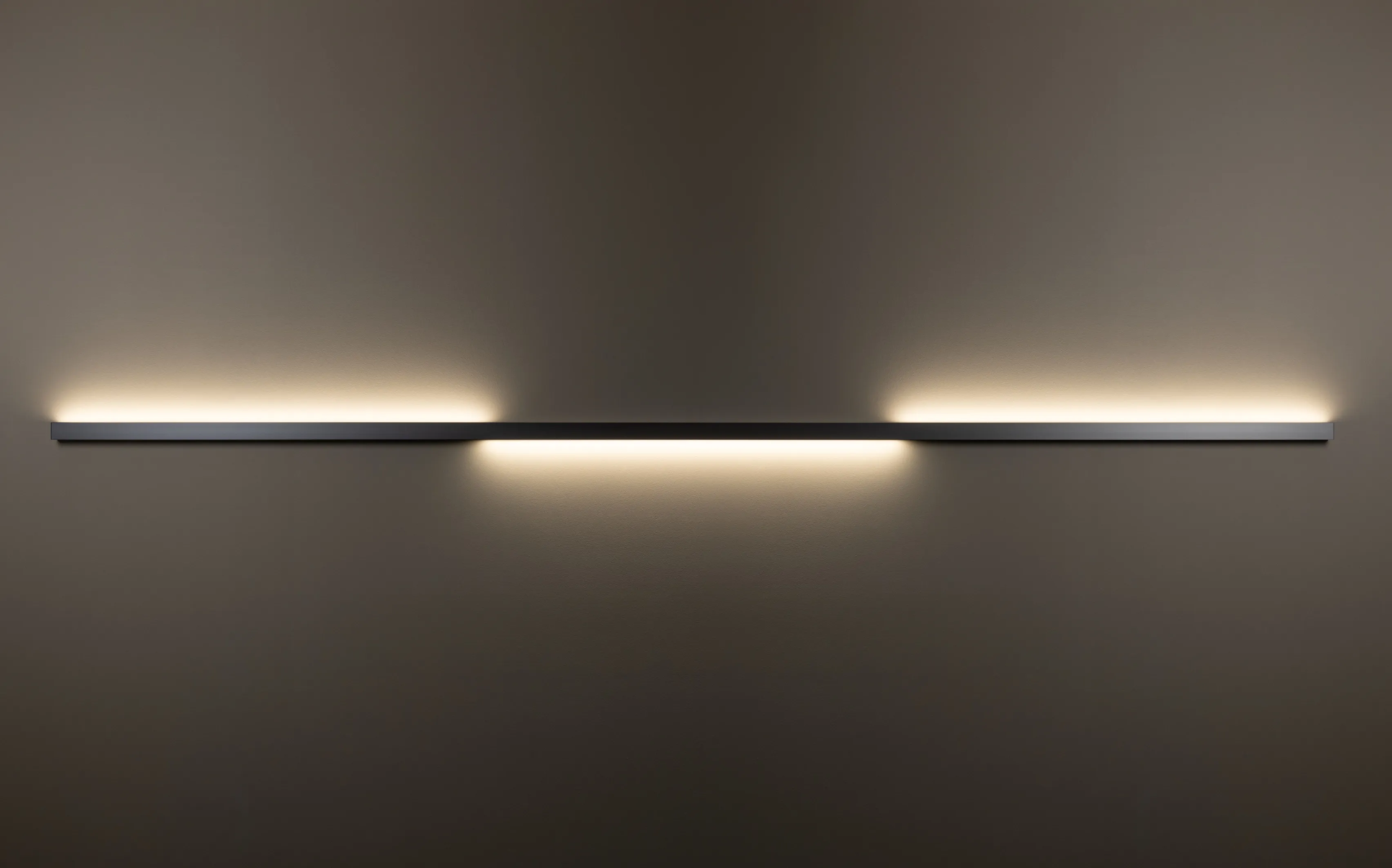 Horizontal installierte Wandleuchte GERA Quadra Wall wirft Licht nach oben und unten auf dunkle Wand.
